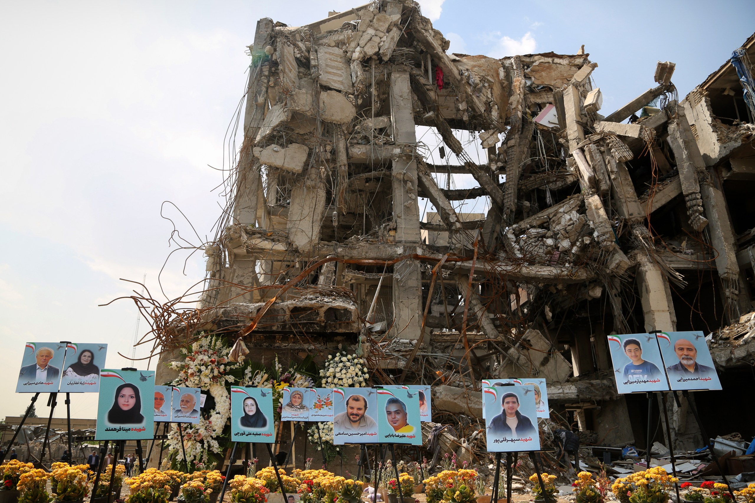 Photos of men, women and children sit on easels in front of the ruins of a residential building.