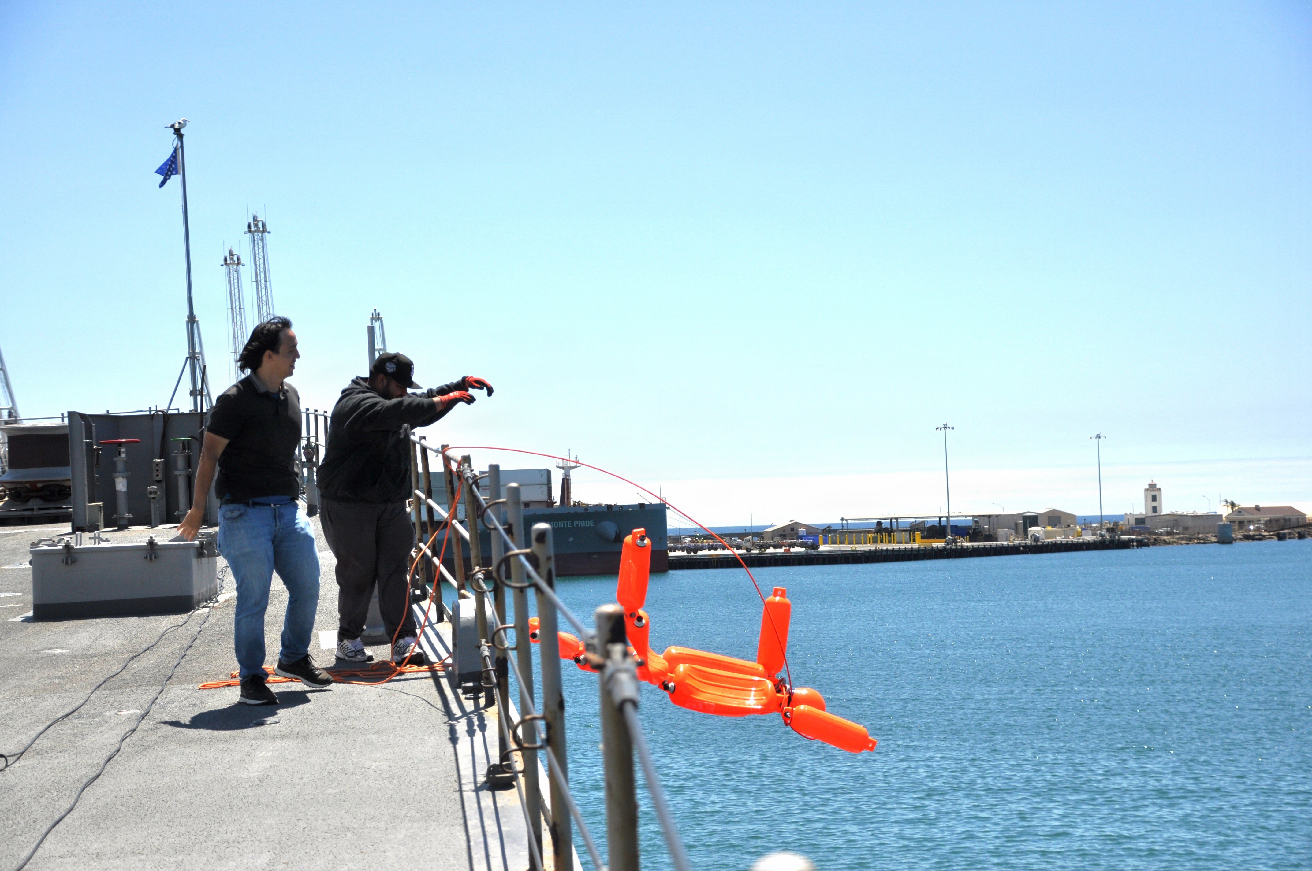 Naval Surface Warfare Center, Port Hueneme Division mechatronics engineer Daniel Lopez (right) tosses a vinyl dummy attached to a rope off the starboard side of the Self Defense Test ship Aug. 14, as Systems Engineer David Dozal looks on. They used the dummy as part of a test of the Man Overboard Detection System designed by their command team.