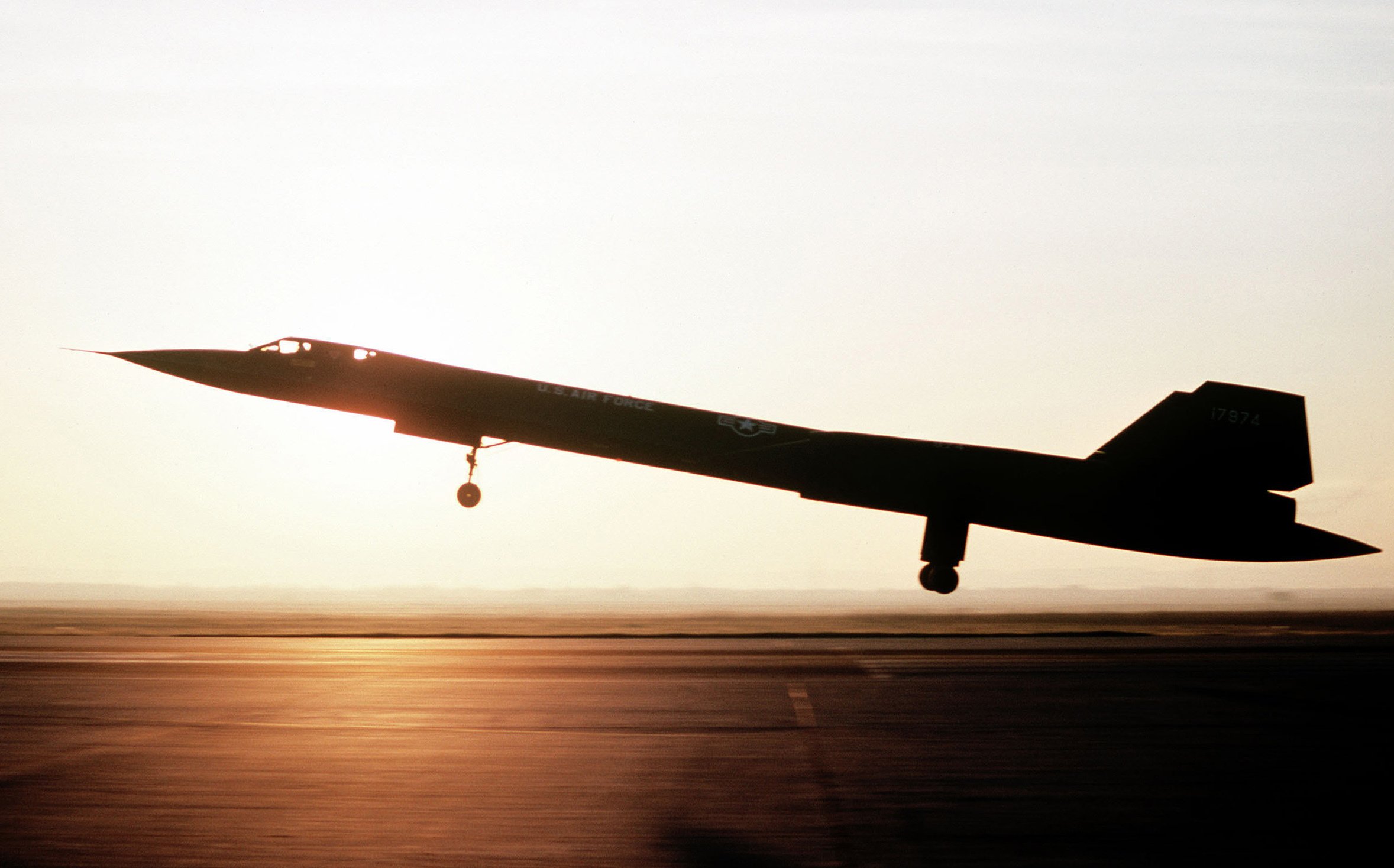 A left side view of an SR-71 aircraft from the 9th Strategic Reconnaissance Wing landing. The aircraft is silhouetted against the sunset.