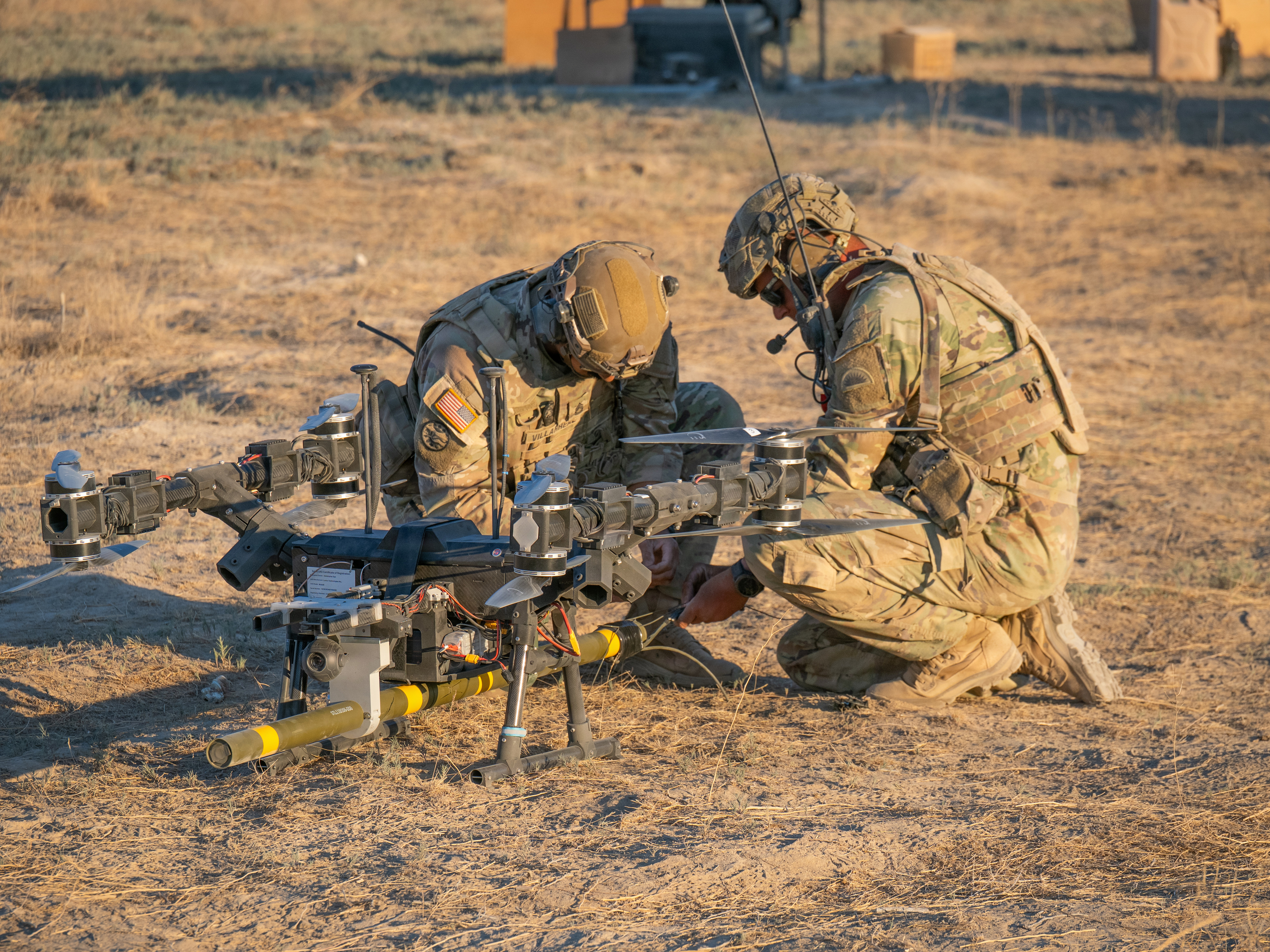 Soldiers prime a live M1A3 Bangalore torpedo by connecting shock tube to the charge before a drone-delivered breach attempt against a concertina wire obstacle June 22, 2026. (Maj. W. Chris Clyne/Army National Guard)