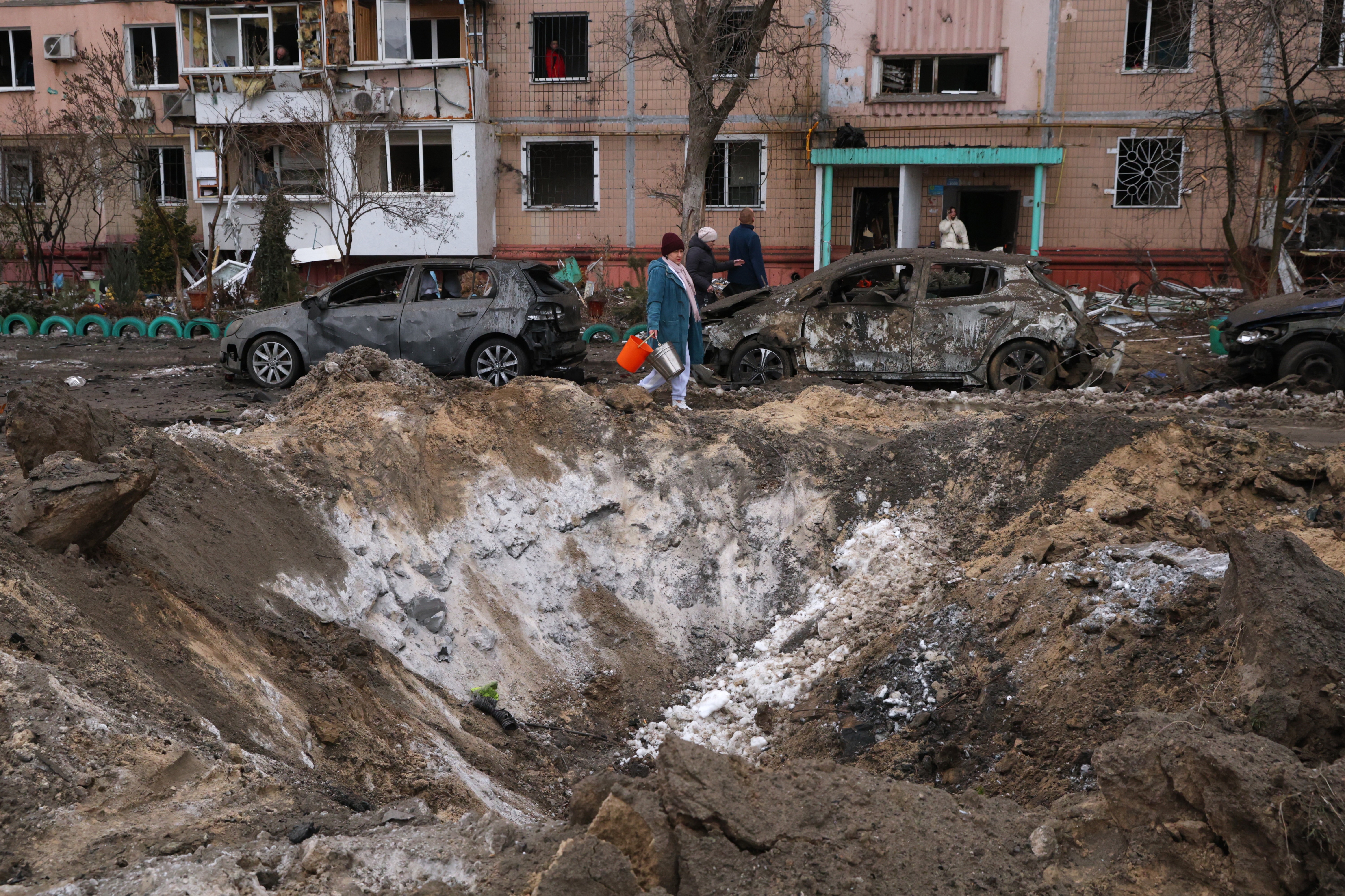 People pass a crater and damaged cars near an apartment building after a Russian attack in Zaporizhzhia, Ukraine, on Wednesday. (Kateryna Klochko/AP)