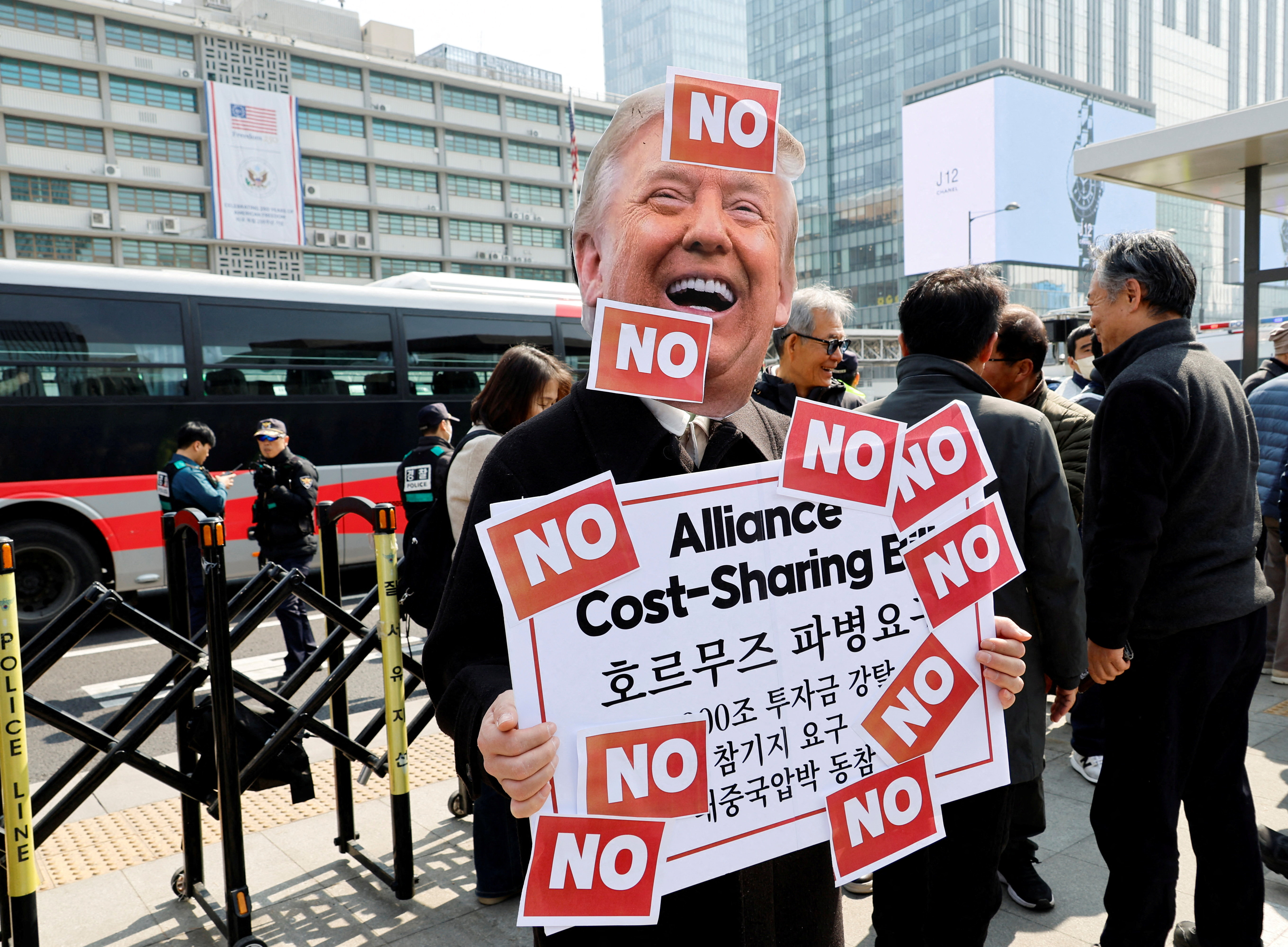 An activist wearing a cutout mask depicting U.S. President Donald Trump is pictured during a rally against the U.S. demand for South Korea to deploy troops to the Strait of Hormuz, outside the U.S. embassy in Seoul, South Korea, March 16, 2026. (Reuters/Kim Soo-hyeon)