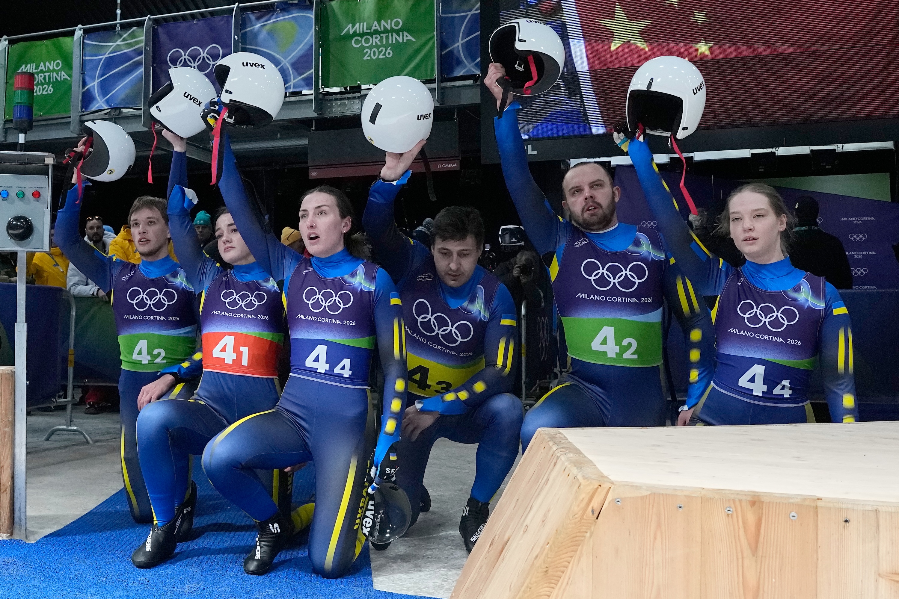 Ukraine's Yulianna Tunytska, Olena Stetskiv, Oleksandra Mokh, Nazarii Kachmar, Ihor Hoi and Andriy Mandziy kneel during the luge relay competition at the 2026 Winter Olympics, in Cortina d'Ampezzo, Italy, Feb. 12, 2026. (Alessandra Tarantino/AP)