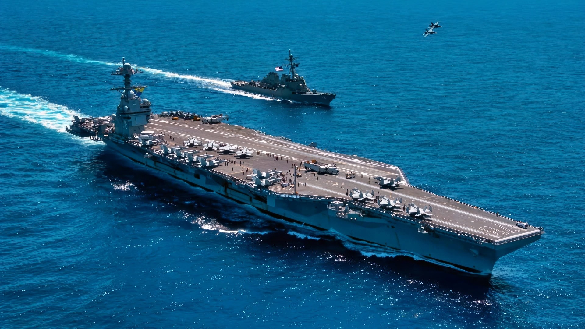 一架F/A-18F超级大黄蜂，隶属于213攻击战斗机中队的“黑狮”，以及一架F/A-18E超级大黄蜂，隶属于87攻击战斗机中队的“金色战士”，在世界上最大的航空母舰——杰拉尔德·R·福特号（CVN 78）和阿利·伯克级导弹驱逐舰马汉号（DDG 72）上空飞行，2025年4月11日。杰拉尔德·R·福特航母打击群正在大西洋进行综合海军作战训练。综合训练单位演习（COMPTUEX）是联合部队最复杂的综合训练活动，为海军特遣队准备持续的高端联合和联合作战。综合海军训练为美国的民选领导人和指挥官提供了高能力的部队，以威慑对手，支撑美国的安全和经济繁荣，并向盟友和合作伙伴提供保障。（美国海军照片，由二级通讯专家麦克斯韦·奥洛斯基拍摄）
