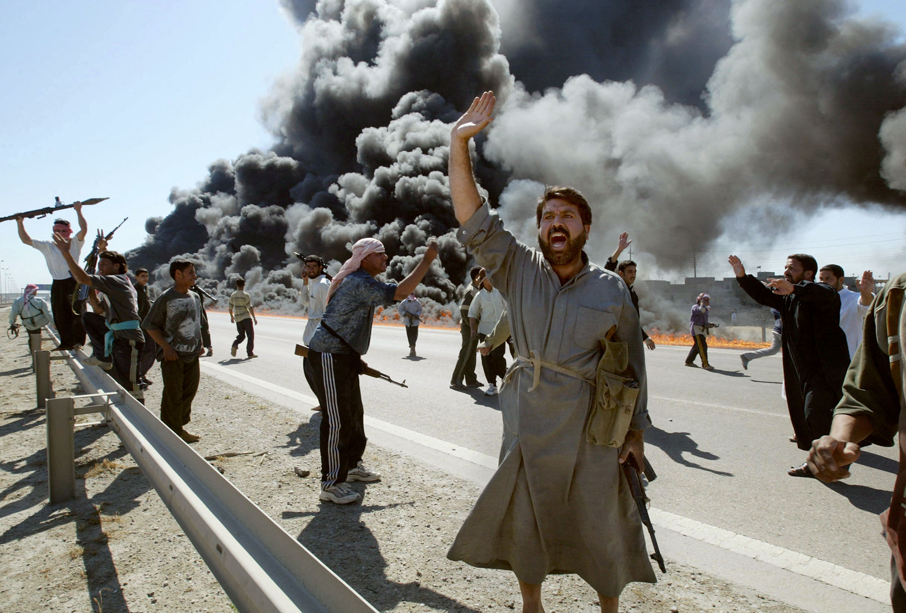 Iraqi Sunni Muslim insurgents celebrate in front of a burning U.S. convoy they attacked earlier on April 8, 2004, on the outskirts of the flashpoint town of Fallujah. (Karim Sahib/AFP via Getty Images)